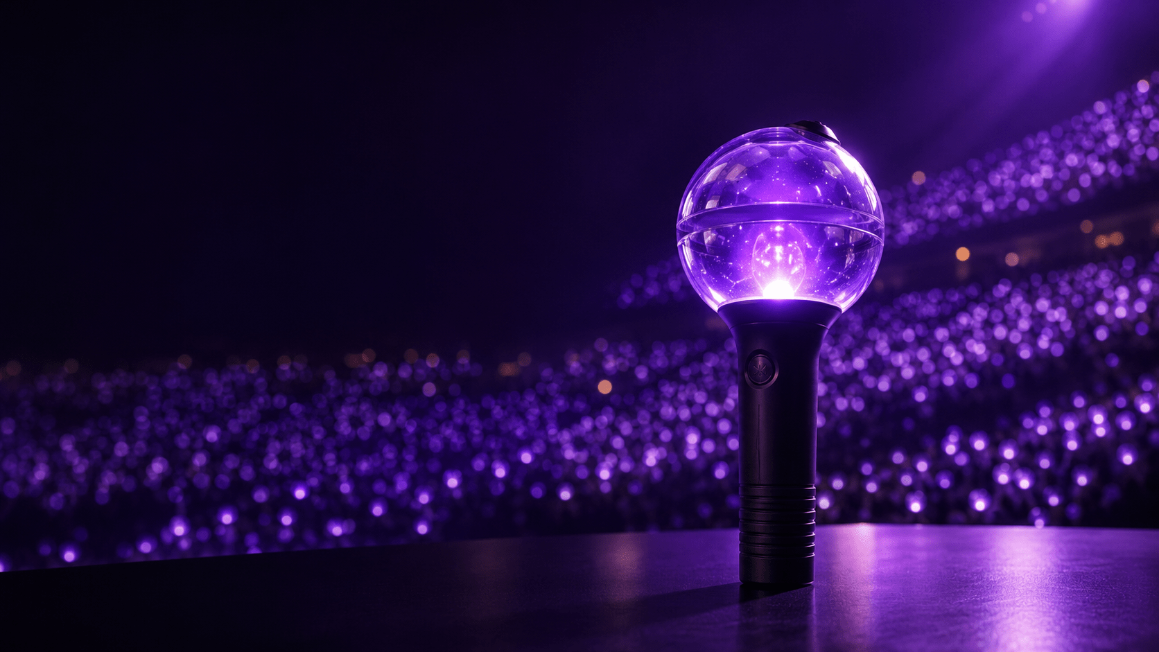 A hero product shot of a spherical globe-shaped K-pop concert lightstick — clear domed top over a matte-black cylindrical handle with a subtle ribbed grip — glowing with a soft purple-violet light from within. The lightstick stands slightly off-center on a dark reflective surface. Behind it, a dreamy bokeh sea of thousands of matching purple lights fills a darkened concert arena, softly out of focus. Cinematic studio lighting with a gentle purple rim light and a cool highlight on the glass dome. Premium, editorial, high-detail, photorealistic. Moody dark background with rich purple and deep-navy tones, a touch of warm glow. Clean negative space in the upper-left third for a title overlay. 16:9, high resolution.