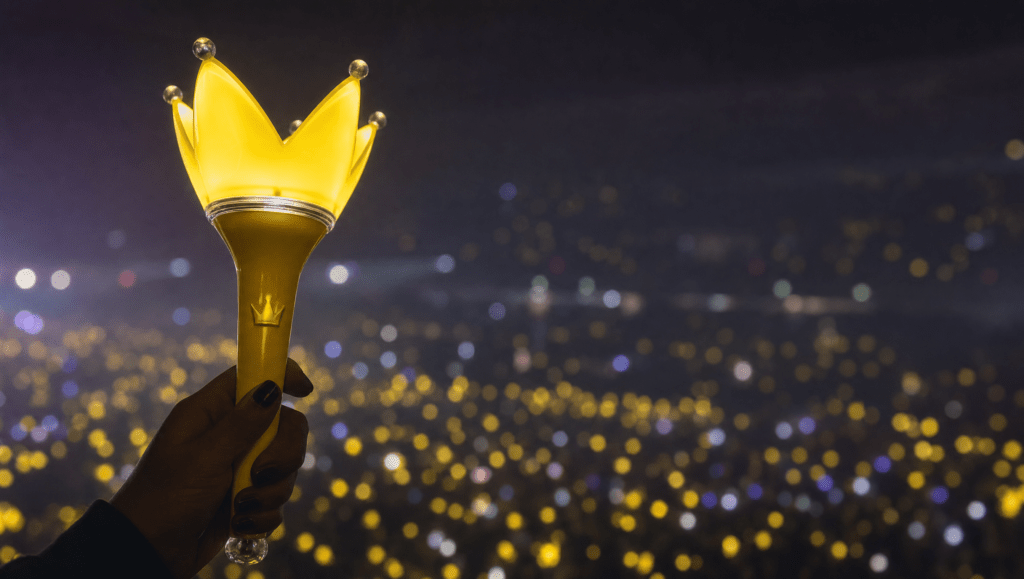 Glowing yellow BIGBANG Bang Bong lightstick with crown top held up in a dark concert arena