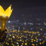 Glowing yellow BIGBANG Bang Bong lightstick with crown top held up in a dark concert arena